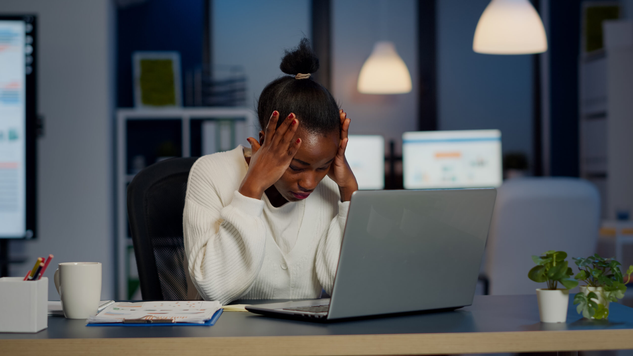 Stressed african businesswoman suffering from headache at work doing overtime late night. Exhausted tensed worker coping with migraine, emotional stress concept feeling pain working at laptop